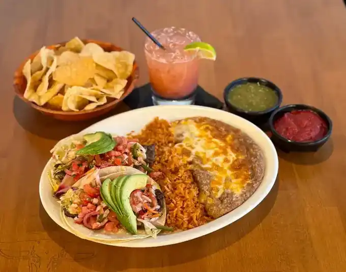 A plate under shredded lettuce and cheese with chips, salsas and a margarita on a Mi Casa table
