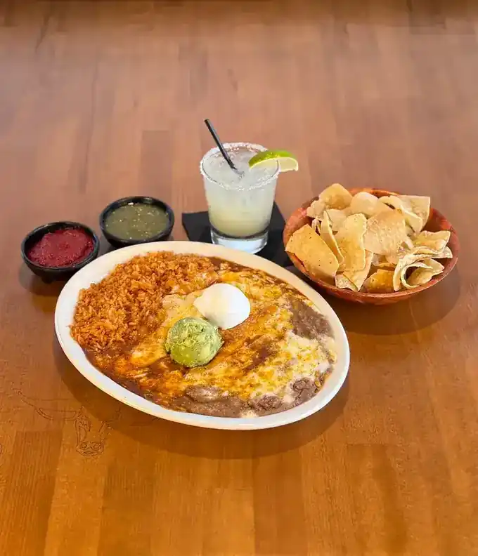 A combination plate with tacos, an enchilada, rice and beans beside chips and a margarita