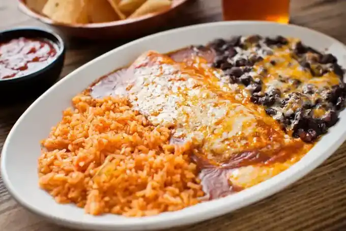 Enchiladas under melted cheese with rice and beans on a Mi Casa plate