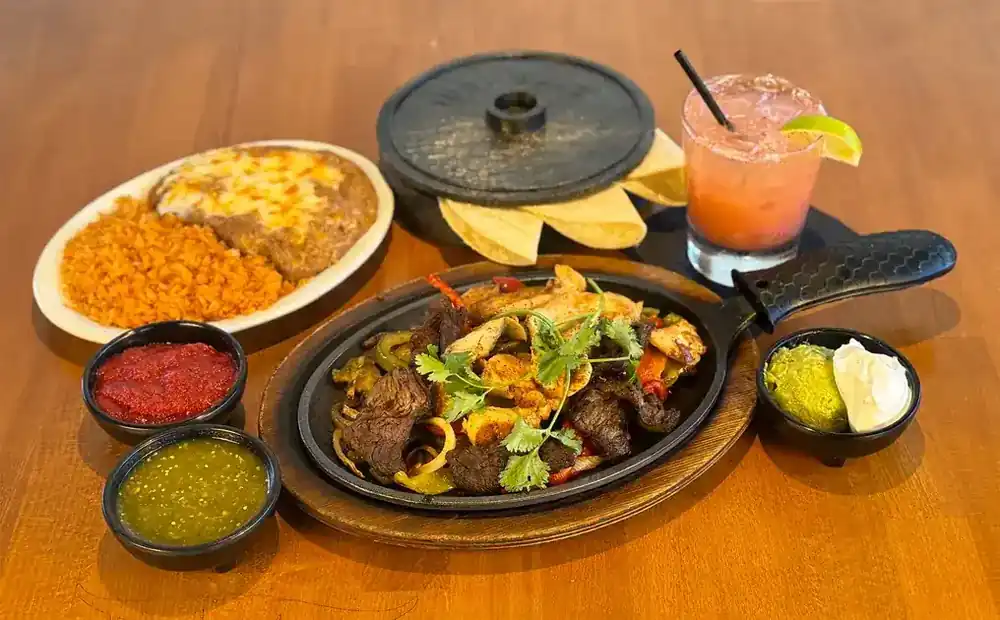 Steak and chicken fajitas on a cast iron skillet with salsas, guacamole and a margarita