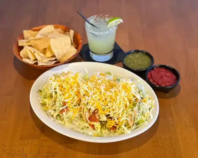 A strawberry margarita and a lime margarita beside a plate of tacos