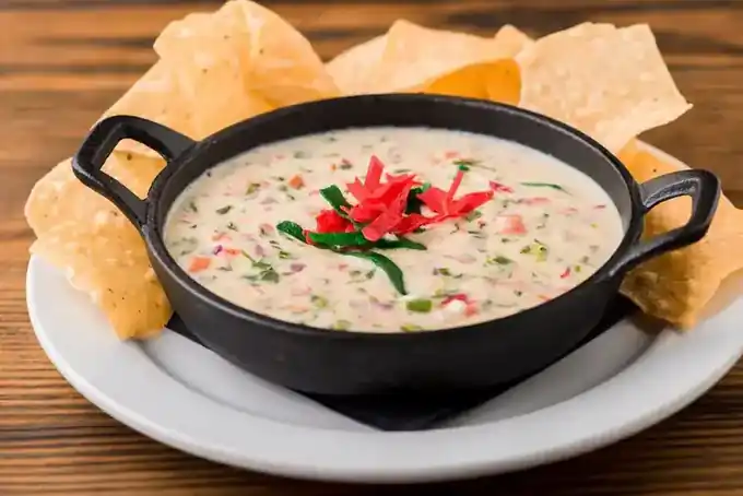 Queso fundido in a black cast iron dish, flecked with peppers and herbs, ringed by tortilla chips