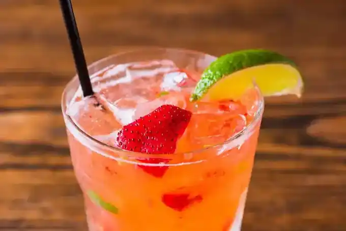 A strawberry and lime drink over ice in a rocks glass on a wooden bar top