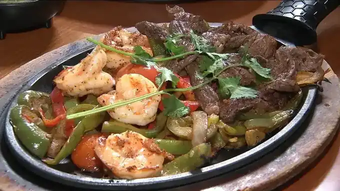 Steak and shrimp fajitas on a cast iron skillet with peppers, onion and cilantro