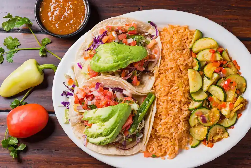 Two tacos with avocado and pico de gallo beside rice and grilled zucchini